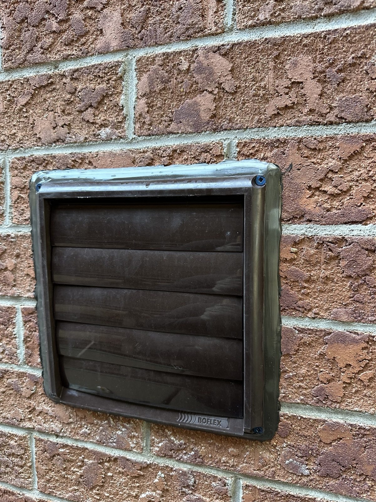 Exterior wall vent sealed where it passes through brick