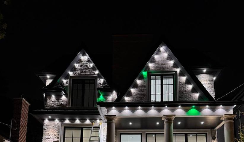 White and green roofline and gable lights on a stone house at night