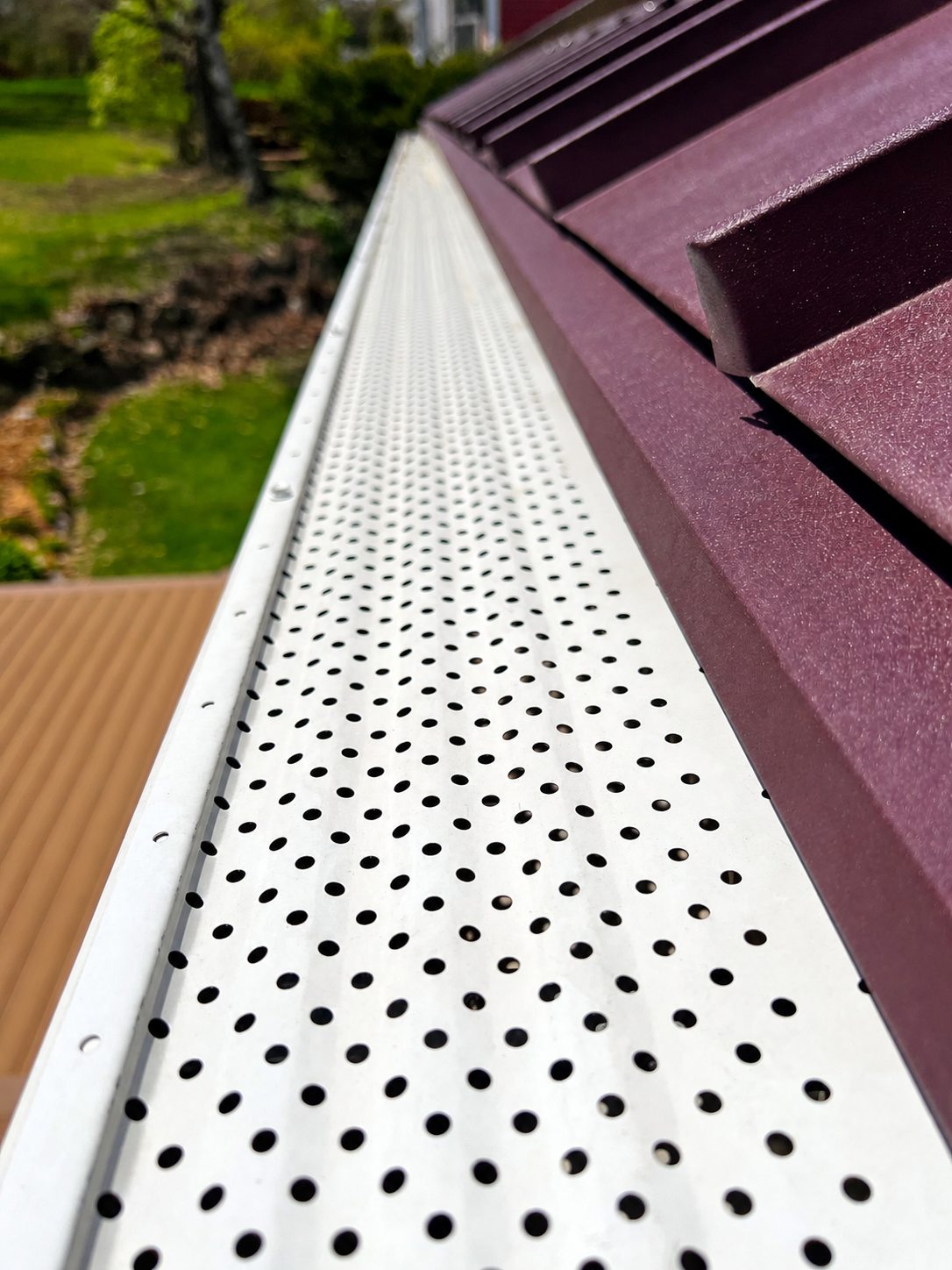 Perforated aluminum leaf filter gutter guard fitted along a roofline