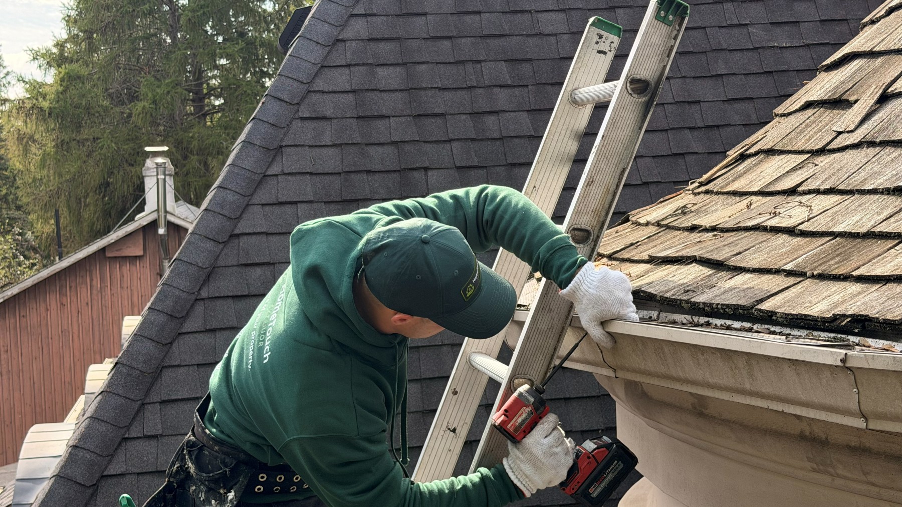 HomeTouch technician on a ladder fastening a gutter at the roof edge with a drill