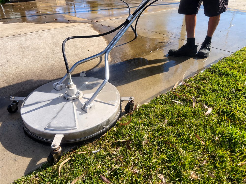 Round surface cleaner attachment in use on a concrete driveway