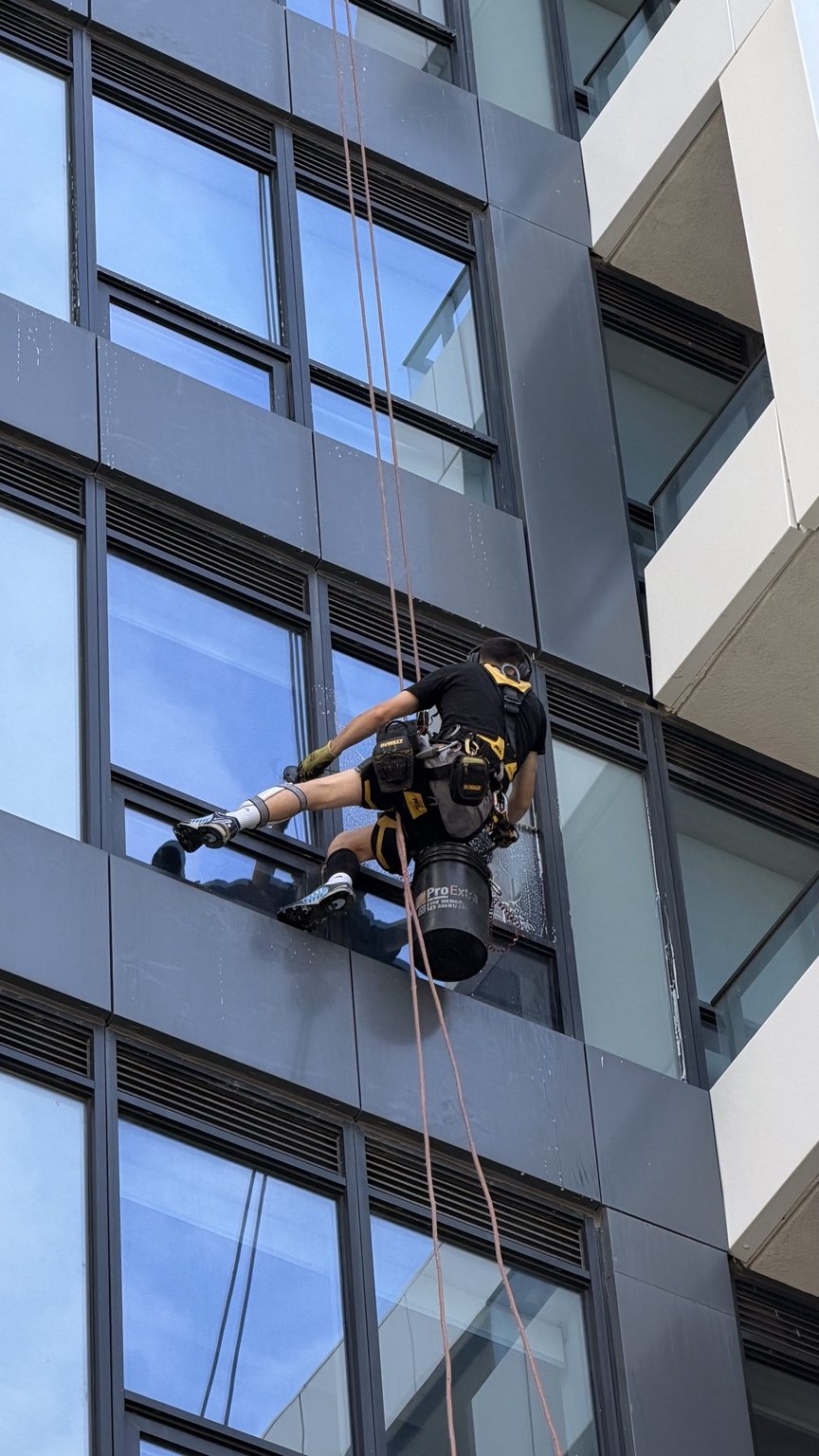 Rope-access window cleaner working on the glass of a tall building