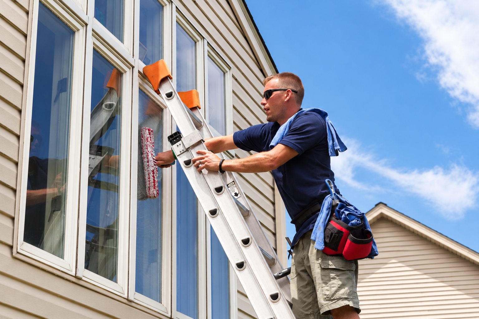 Window cleaner on a ladder washing the upper windows of a house